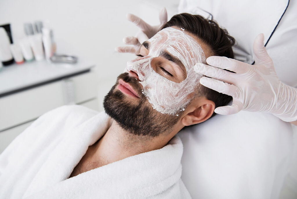 Hands in rubber gloves touching temples of relaxed man in salon