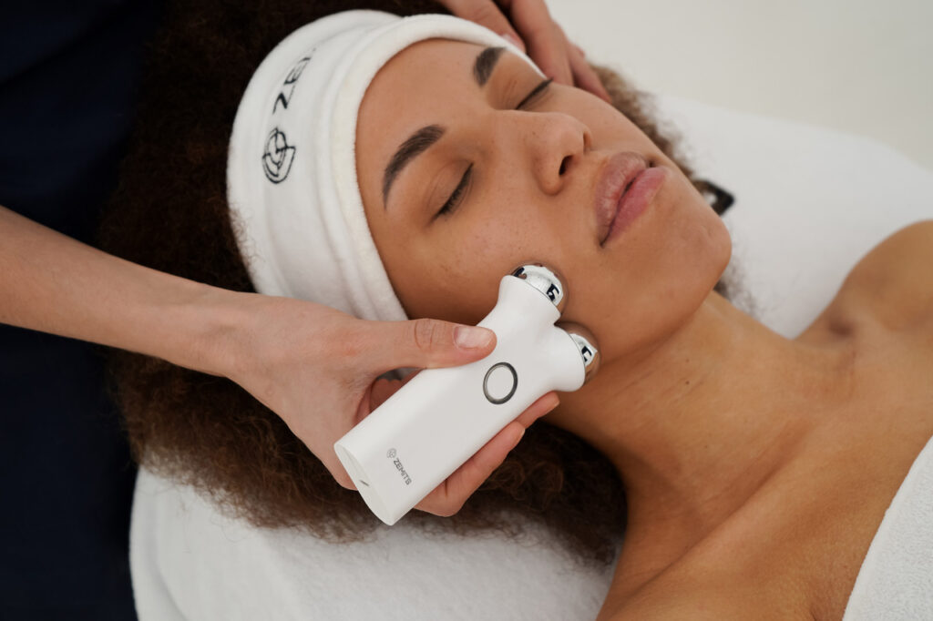 Person receiving a facial treatment with a handheld device while lying on a spa bed.